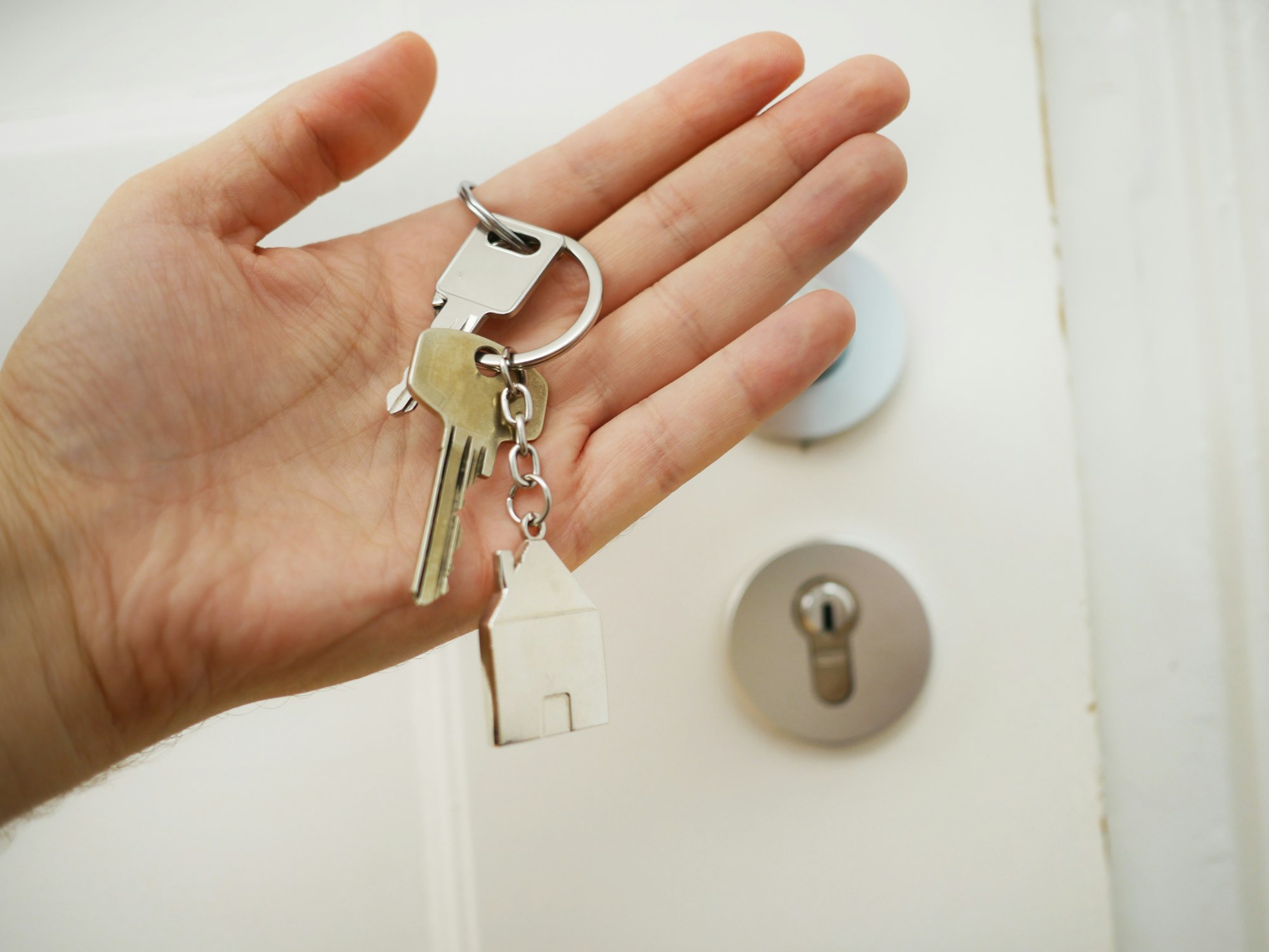 Hand holding house keys beside a front door deadbolt